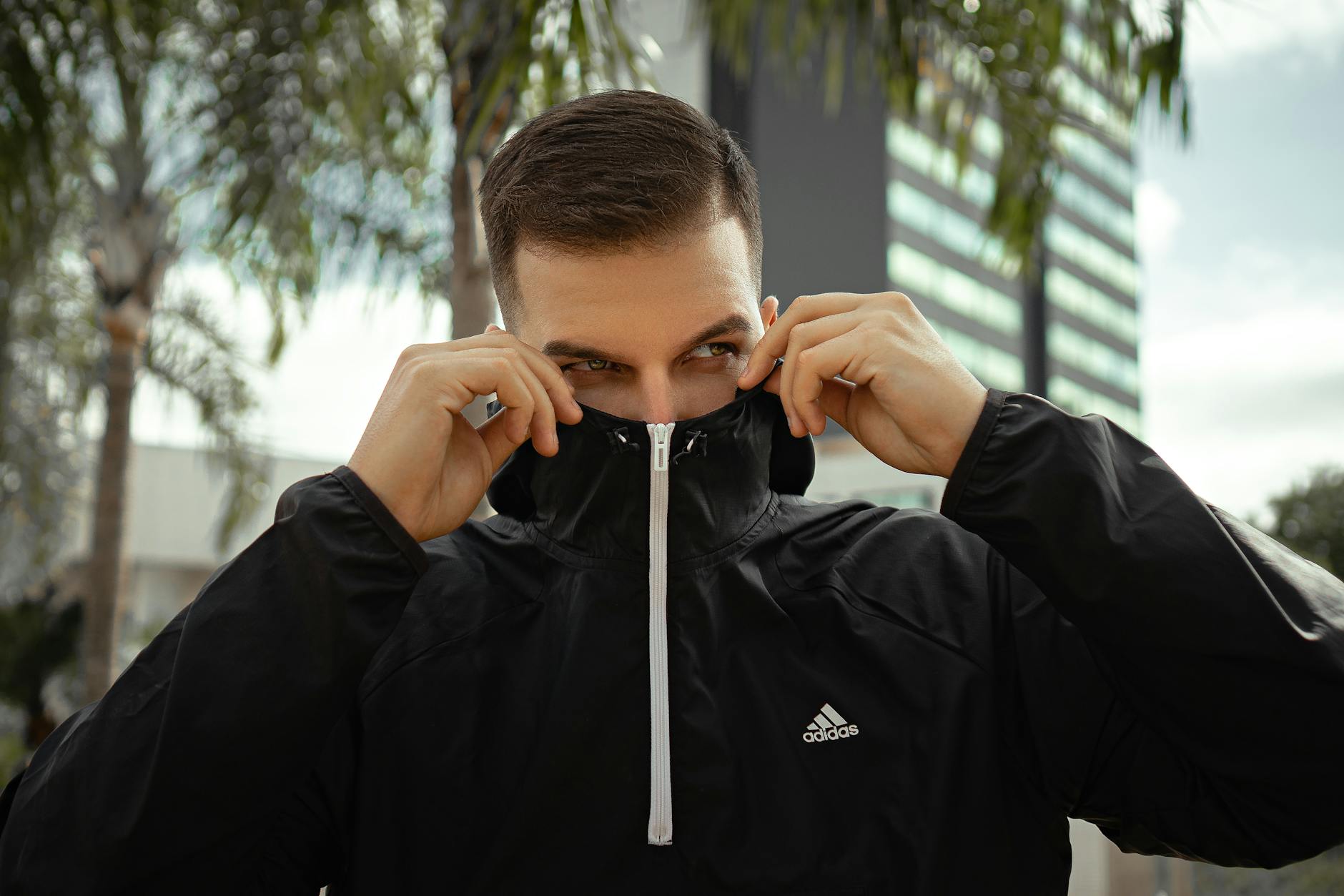 Mężczyzna w czarnej kurtce Adidas poprawia kaptur na ulicy