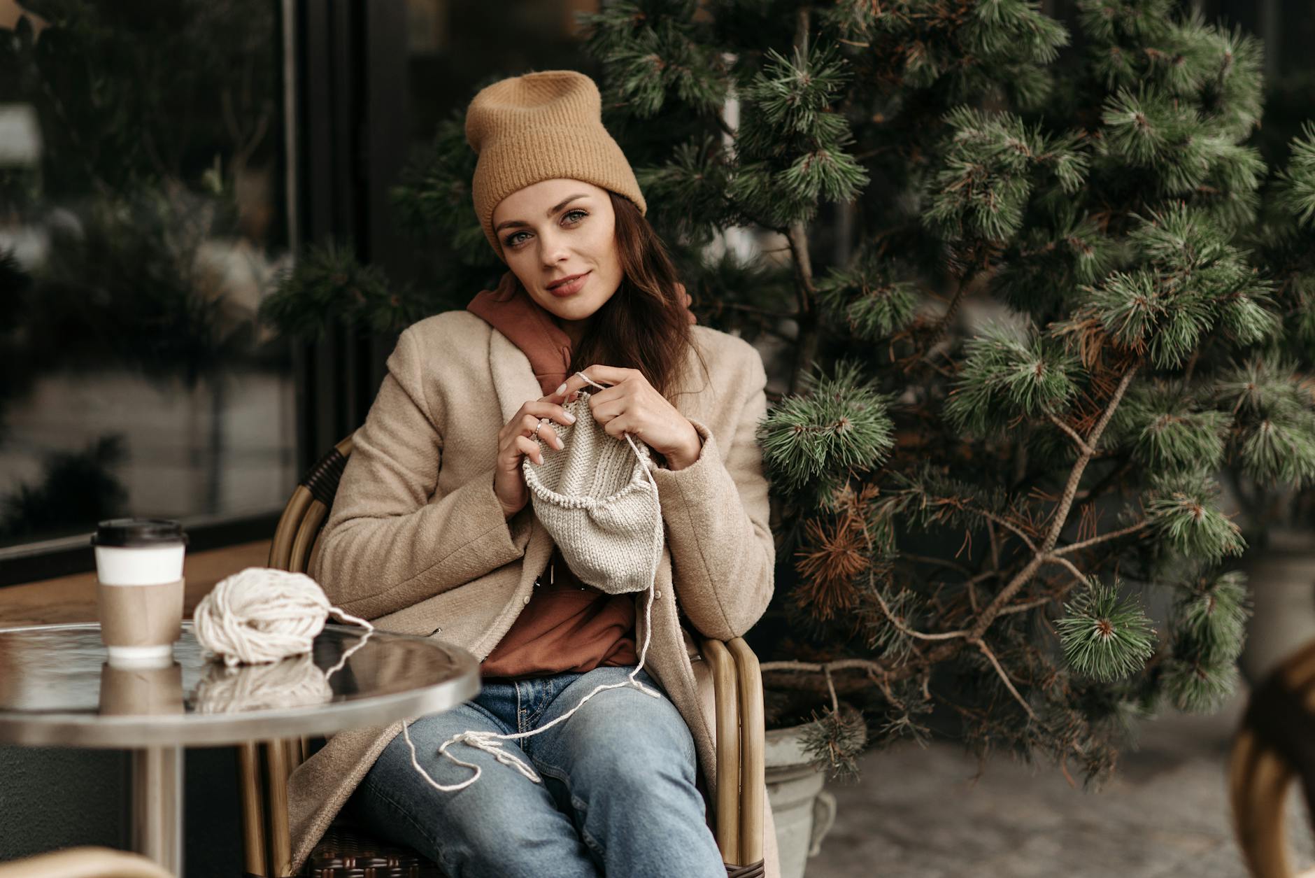 Młoda kobieta dzierga na drutach przy stoliku w kawiarni na zewnątrz