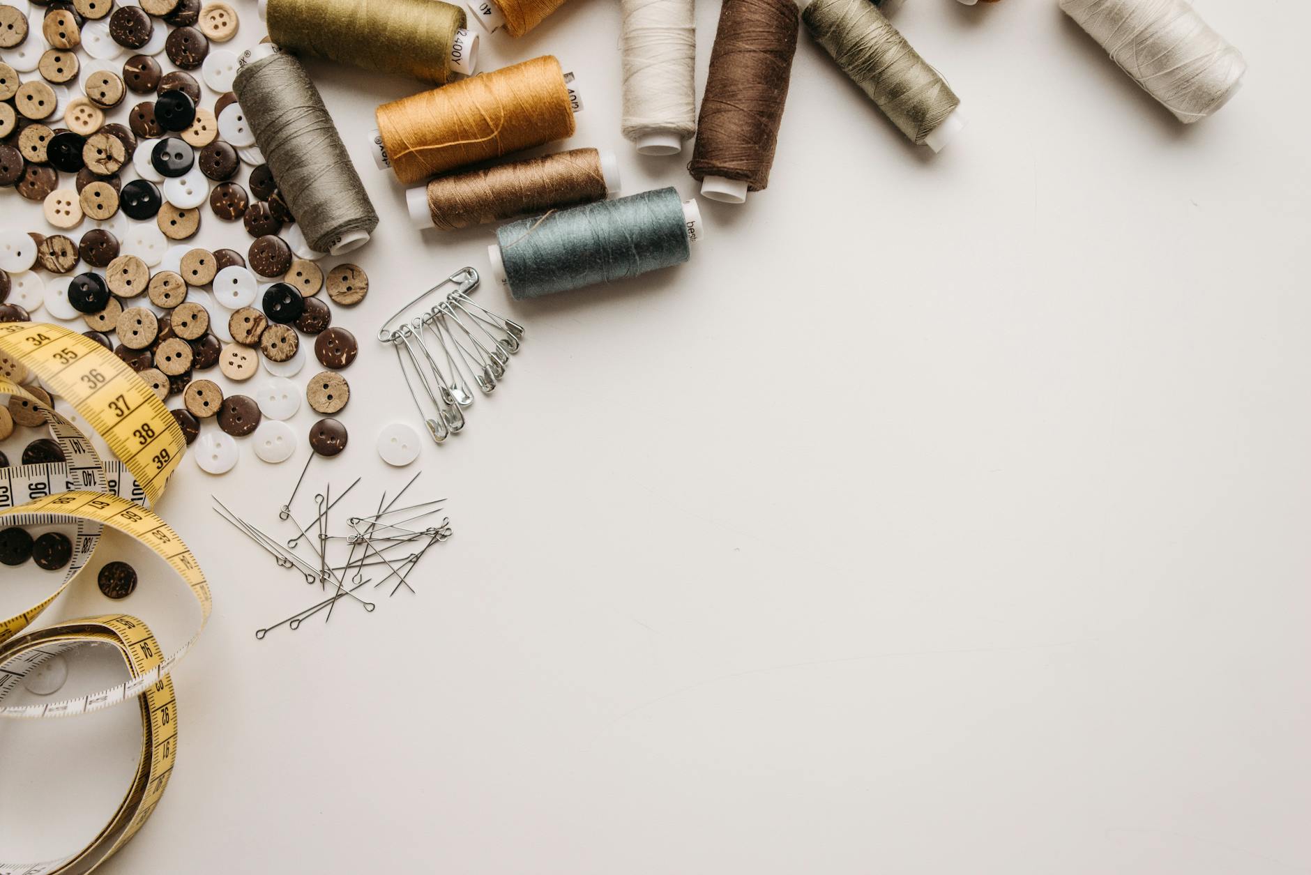 Płasko ułożone nici, guziki i centymetr krawiecki na białym tle