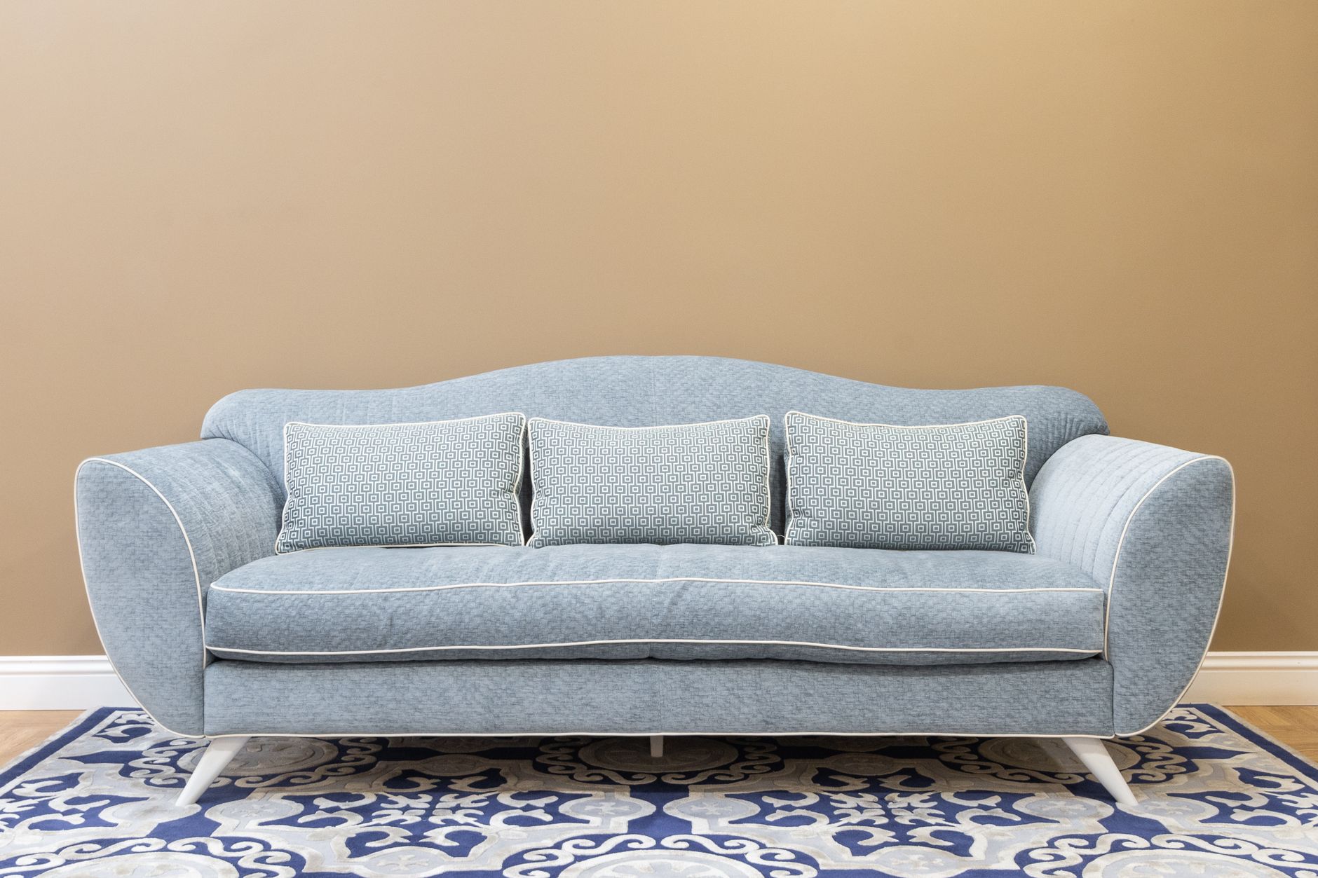 Niebieska sofa z poduszkami na wzorzystym dywanie w nowoczesnym salonie